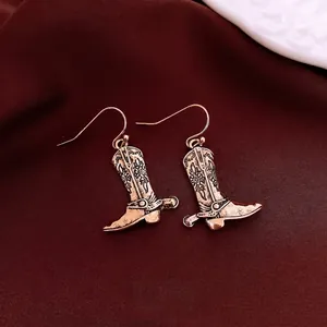 Vintage bronze cowboy boot earrings with floral engraving on deep red fabric background