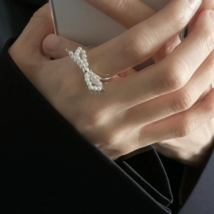 Detail of woven white pearl bow ring on finger with elegant silver metal band