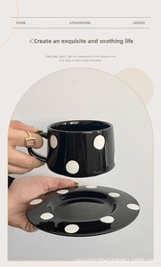 Gros plan d'une main tenant une tasse à café en céramique noire à gros pois blancs