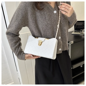 Detail showing white woven leather shoulder bag with gold clasp on an office desk