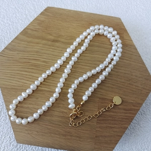 Close-up of natural freshwater pearl necklace with gold lobster clasp on wood stand