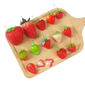 Realistic artificial strawberry models in various sizes and slices on a wooden board