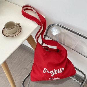 Detail of red canvas tote bag with Bonjour print and striped shoulder strap on a chair