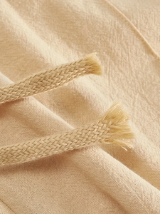 Detailed close-up of light beige linen fabric texture and woven drawstring on casual pants