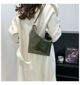 Deep green textured bucket bag with glossy finish shown as a shoulder style on a model