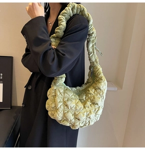 Detail of a green pleated shoulder bag with puffy texture worn by a model in a minimal setting