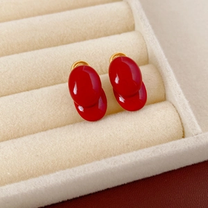 Nahaufnahme eleganter roter ovaler Ohrstecker mit goldenen Metallteilen auf Samt