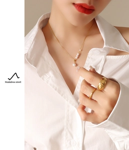 Detail of gold stainless steel necklace with five pearls and matching rings on a model
