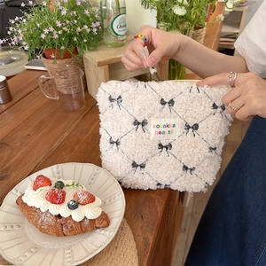 Detail of beige fleece cosmetic bag with black bow pattern and embroidered logo label