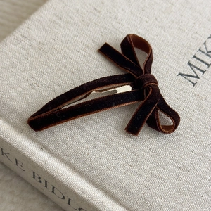 Macro detail of dark brown velvet bow hair clip on a beige textured fabric background