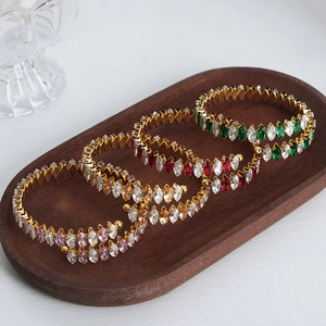 Elegant gold plated open bangles with colorful zircon stones in a walnut wooden tray