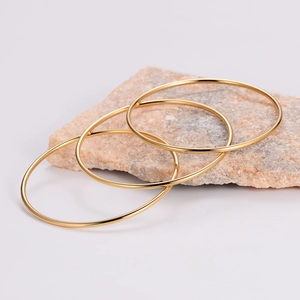 Three-piece set of minimalist polished gold stainless steel bangles on natural stone