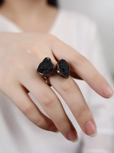 Detailed close-up of a vintage adjustable copper ring with two raw black stones on a finger