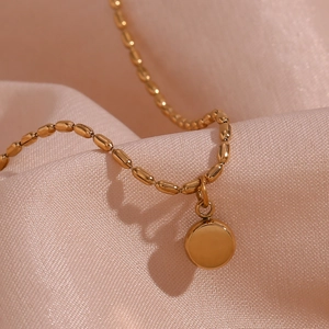 Detail of 18K gold plated beaded chain with a natural stone disc pendant on pink silk