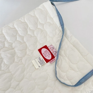 Détail de la texture matelassée blanche avec bandoulière bleue et étiquette colorée