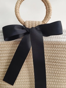 Handwoven straw tote bag featuring round handles and a black decorative silk ribbon