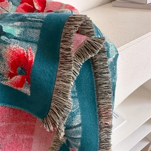 Detailaufnahme der Blumen-Strickdecke mit bunten Mustern und grauen Fransen am Rand