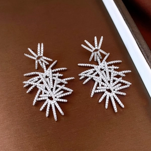 Macro detail of silver starburst drop earrings with zircon crystals on a brown tray
