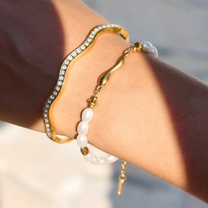 Close-up of 18K gold wave bangle with diamonds and pearl bracelet on a wrist