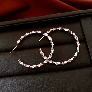 Detail of silver geometric twist earrings displayed on black leather and red silk fabric
