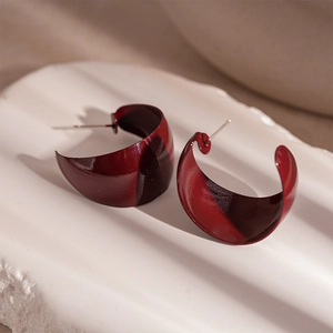 Macro view of polished deep red C-shaped hoop earrings on a white textured stand