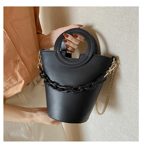 Detail of a chic black bucket bag with a round handle and decorative thick black chain