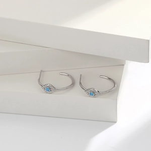 Macro detail of silver C-shaped evil eye earrings with blue opal and white zircons