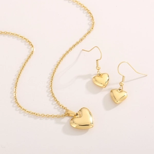 Détail du pendentif cœur doré poli et des boucles d'oreilles cœur assorties sur fond beige