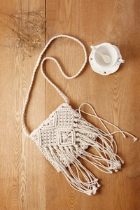 Nahaufnahme der cremefarbenen Macramé-Tasche mit langen Fransen auf holzigem Untergrund