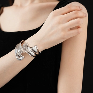 Close-up of wide irregular silver metal bangle on wrist with reflective sculpted surface