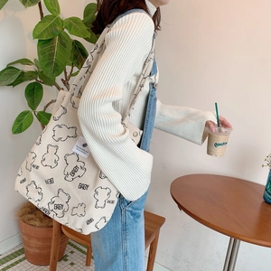 Detail of corduroy shoulder bag with baby bear print worn in a cozy indoor setting