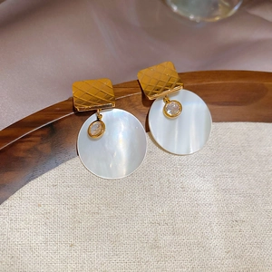 Dettaglio di orecchini placcati oro 24k con madreperla bianca e zirconi scintillanti