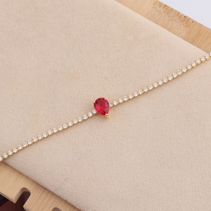 Detailopname van een gouden ketting met een traanvormige rode edelsteen en zirkonia-inleg