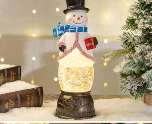 Illuminated Christmas snowman water globe lamp on snowy background with festive decor