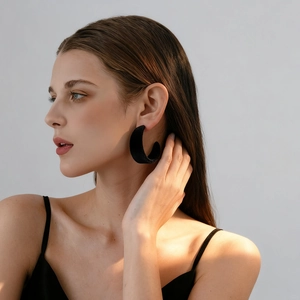 Detail of matte black flocked C-shaped hoop earring worn by a model with soft shadows