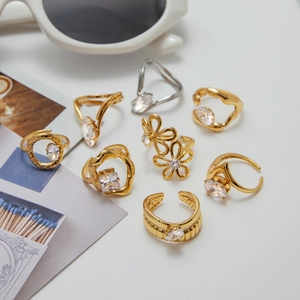 Flat lay of gold and silver zircon rings with sunglasses and artistic postcard accents
