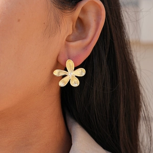 Detail of golden flower earring with brushed metal texture and tiny zircon inlay