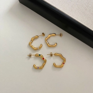 Macro view of C-shaped wavy gold earrings with clear and multicolor rhinestones