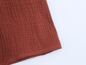 Detail of embroidered hemline on a rust red cotton summer dress with textured seersucker fabric