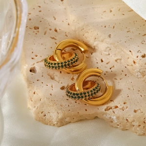Golden double hoop earrings with green zircon accents on textured stone and silk