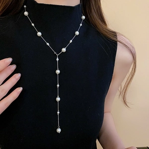 Detail of a long Y-shaped faux pearl necklace on a black turtleneck sweater
