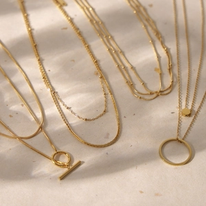 Minimalist 18K gold-plated multilayer necklace collection displayed on artistic paper