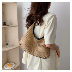Detail of woven tote bag with black leather trim worn on shoulder in home setting