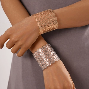Dettaglio di bracciali a polsino color oro e argento con motivi floreali e cuori traforati