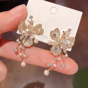 Detailed close-up of golden butterfly earrings with rhinestones and pearl tassels on 925 silver pins