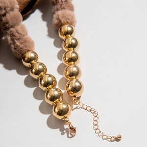Gros plan des perles dorées et pompons bruns d'un collier de Noël avec un fermoir mousqueton