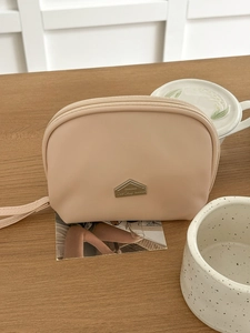 Detail of apricot semi-circle mini lipstick pouch with metal tag and wrist strap on wood table