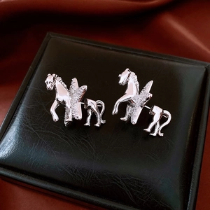 Macro shot of silver pegasus earrings with sparkling white zircons on black leather