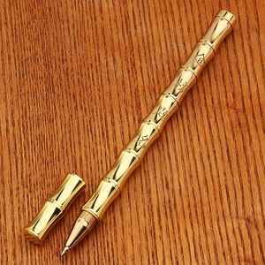 Macro detail of brass bamboo-shaped pen with engraved Chinese characters on wood background