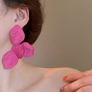Close-up of vibrant rose red matte floral stud earring worn by a model